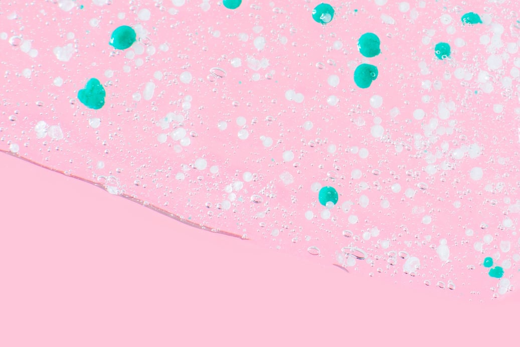 Smeared transparent gel with blue granules. On a pink background.